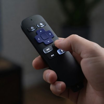 Hand holding a backlit Roku voice remote, buttons in sharp focus